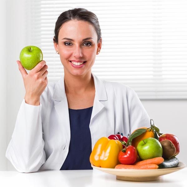 Mujer sosteniendo una manzana junto a un plato con más fruta